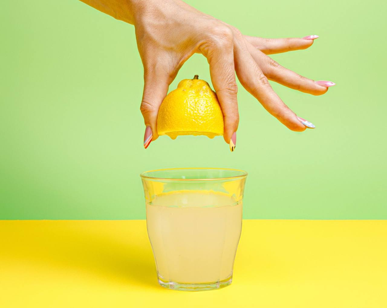 Hand presst eine halbe Zitrone über einem Glas Limonade aus